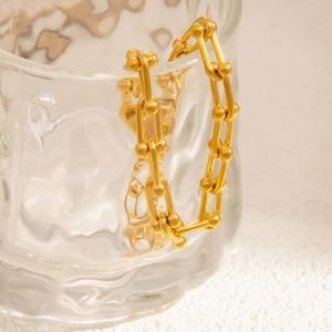 Detailed macro view of 18k gold plated U-shaped link chain bracelet on textured glass