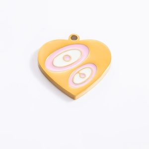 Macro shot of gold heart pendant with pink enamel eye detail and polished finish
