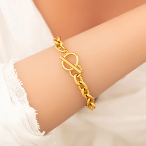 Detail of a gold OT-clasp chain bracelet on a wrist with polished minimalist metal rings