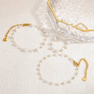 Détail de trois bracelets de perles avec breloques cœur dorées sur une surface en pierre