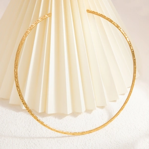 Close-up of golden hammered finish stainless steel choker on a minimalist white stone base