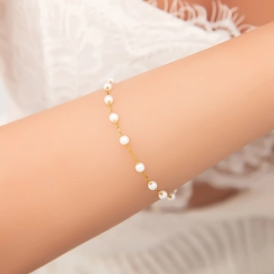 Vue détaillée d'un bracelet en perles dorées porté au poignet avec chaîne délicate