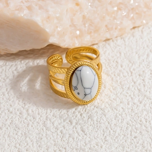Detail view of gold stainless steel layered ring with white marble stone on sand background