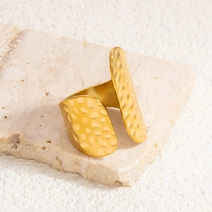 Detailed view of wide gold open ring featuring unique hammered metal texture and polished edges