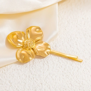 Close-up of golden four-petal flower hair clip with textured petals on satin background