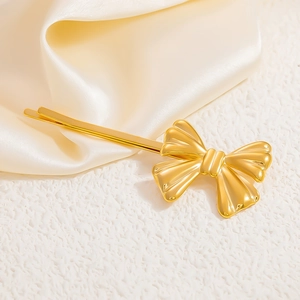 Detailed macro of a gold bow-shaped hair clip on silk fabric with pearl accents