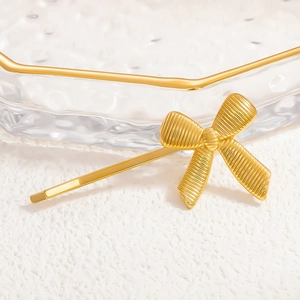 Detailed close-up of golden metal bow hair clip with textured vertical relief on tray