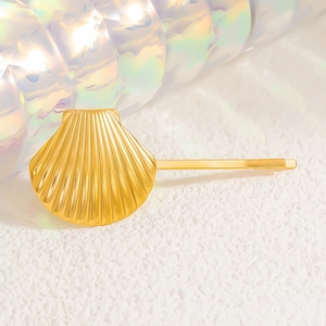 Close-up of golden shell-shaped hair clip with polished finish on sandy background