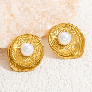 Close-up of 18k gold-plated wavy earrings with pearls on natural white sand and stones