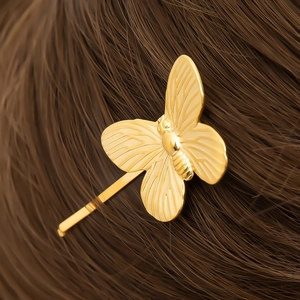 Close-up of golden 18K butterfly hair clip with detailed wing texture on brown hair