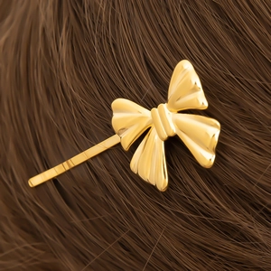 Detail of 18K gold stainless steel bow hair clip with mirror finish on dark hair background