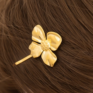 Detailed close-up of a golden four-petal flower hair clip on dark brown hair