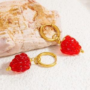 Détail de boucles d'oreilles fraises en verre rouge avec créoles dorées sur fond blanc