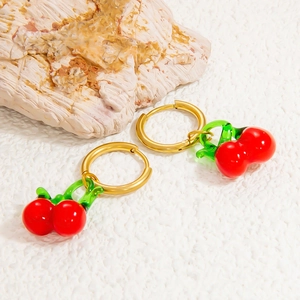 Détail de boucles d'oreilles cerises en verre avec anneaux dorés sur fond de pierre blanche