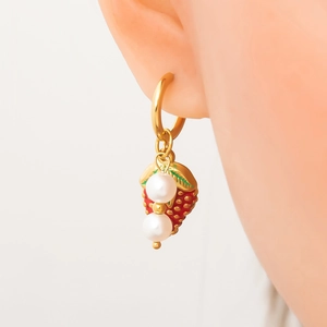 Détail de boucles d'oreilles fraise dorées avec finition rouge et perles sur modèle