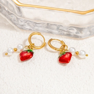 Détail de boucles d'oreilles fraises dorées avec perles blanches et pendentifs rouges