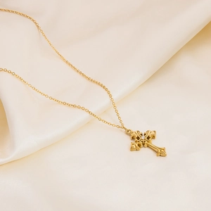 Detailed close-up of a golden cross pendant with vintage patterns on a beige silk background