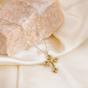 Close-up of golden cross pendant with zircon and baroque pearls on silk fabric