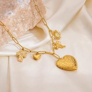 Detail of gold paperclip chain necklace with heart locket, cross, and sun charms on silk