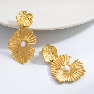 Detalle de pendiente dorado en forma de abanico con textura cepillada y perla blanca central