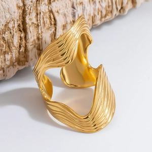 Close-up of golden wide open cuff bracelet with organic wavy texture on a natural stone base