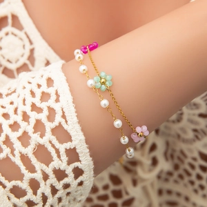 Double-layered gold pearl bracelet with colorful floral charms on female wrist