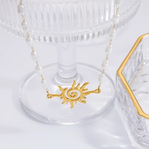 Detailed close-up of a pearl necklace with a golden sun pendant on a glass tray