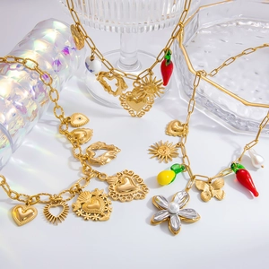 Detail of gold charm necklace with pearls, heart, and fruit pendants on glass tray