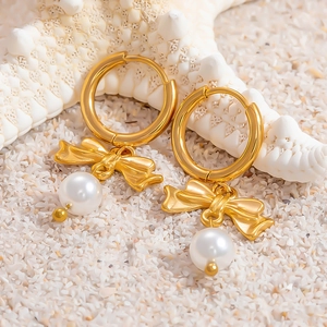 Dettaglio di orecchini in oro 18k con fiocco e perla su stella marina e sabbia