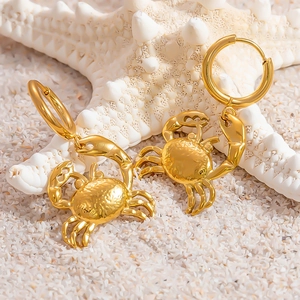 Dettaglio di orecchini a forma di granchio in oro 18k con texture martellata su sabbia bianca