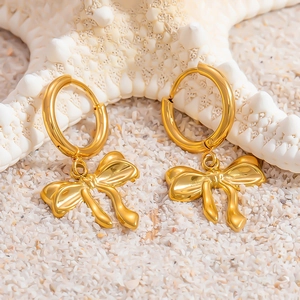 Dettaglio ravvicinato di orecchini a fiocco placcati in oro 18k su sabbia bianca fine