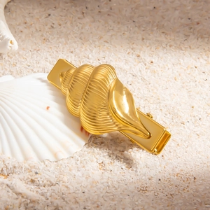 Détail macro d'une barrette coquillage en or 18k posée sur le sable blanc