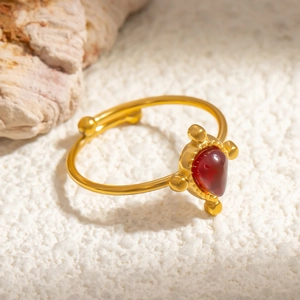 Adjustable gold stainless steel ring with red pear-cut obsidian stone on stone background