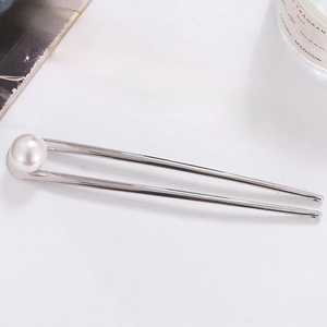 Detail view of a silver U-shaped hair pin with a single white pearl on a white surface