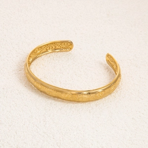 Detail of 18K gold-plated cuff bracelet featuring embossed evil eye patterns and texture