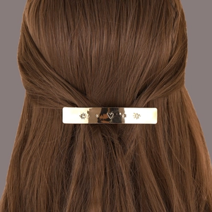 Détail d'une pince à cheveux rectangulaire dorée avec motifs de cœurs et d'étoiles