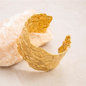 Detail of a wide gold-plated cuff featuring an irregular hammered lava texture