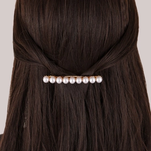 Detailed view of ten white pearls on a gold barrette hair clip in brown hair