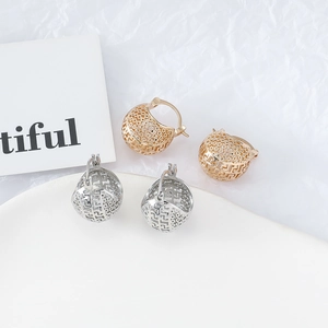 Détail de boucles d'oreilles boules évidées dorées et argentées avec motifs en H