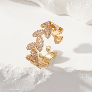 Adjustable leaf-shaped golden ring with pavé zircon stones on white stone background