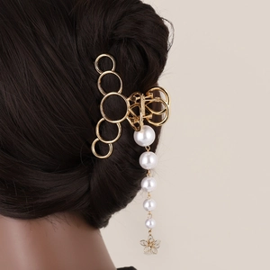 Détail d'une pince à cheveux dorée avec pompon en perles et pendentif fleur ajourée