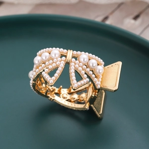 Elegant golden butterfly hair claw with white pearls on a minimalist dark green base