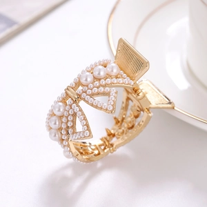 Elegant gold bow hair claw clip featuring inlaid white pearls on a decorative white plate