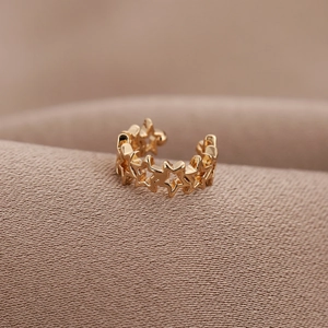 Minimalist U-shaped gold star ear cuff clip earring on a textured fabric surface