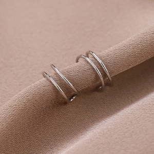 Nahaufnahme von silbernen dreilagigen Ohrmanschetten auf elegantem beige Satin