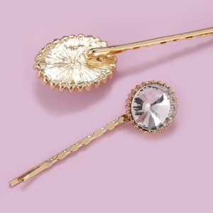 Elegant pair of golden hair clips with large clear rhinestones on a soft pastel background