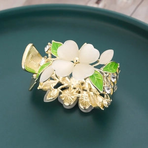 Pince à cheveux fleurie avec monture dorée, pétales blancs et feuilles vertes sur plat en céramique