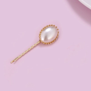 Detailed close-up of a gold metal hair clip featuring a white oval faux pearl inlay