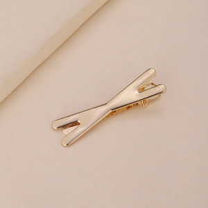 Détail d'une pince à cheveux minimaliste dorée en forme de X avec une finition polie