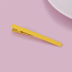 Detail view of a bright yellow matte metal hair clip with anti-slip teeth on pink background